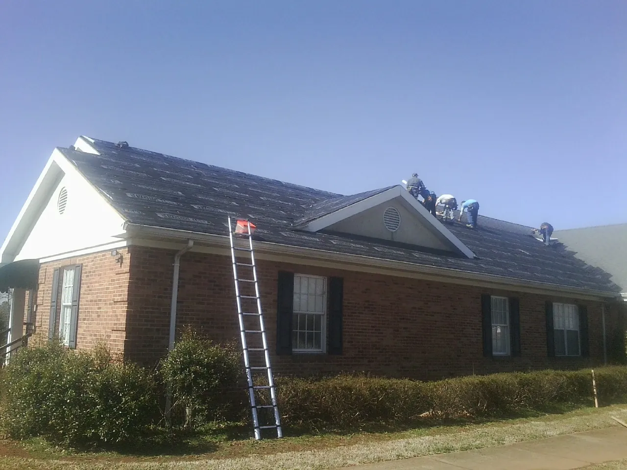 Crew tearing shingles off a brick ranch roof with a ladder set — Metal Roof Repair work by our crew in Warrenville