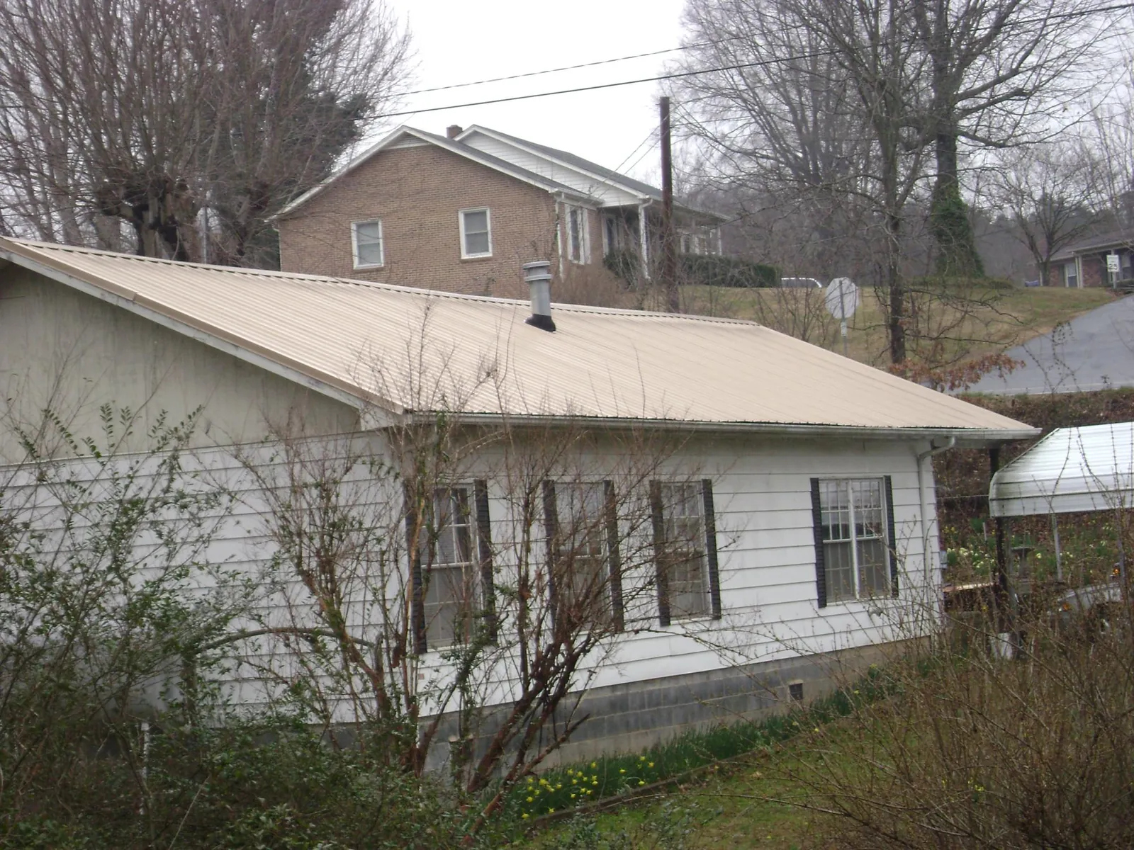 Tan metal roof on a white sided house set into a hillside — Commercial Roofing by Roofing Brothers in Warrenville